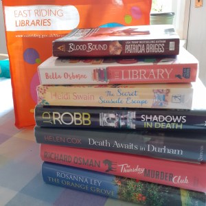 Photo of a stack of books form the library including The Library by Bella Osborne, The Thursday Murder Club by Richard Osman